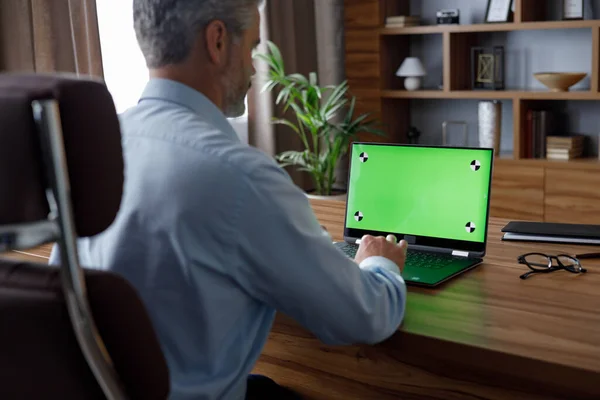 Businessman working with laptop green screen with tracking markers. Male worker talking and listening during video conference with chroma key computer screen. Over shoulder laptop screen view
