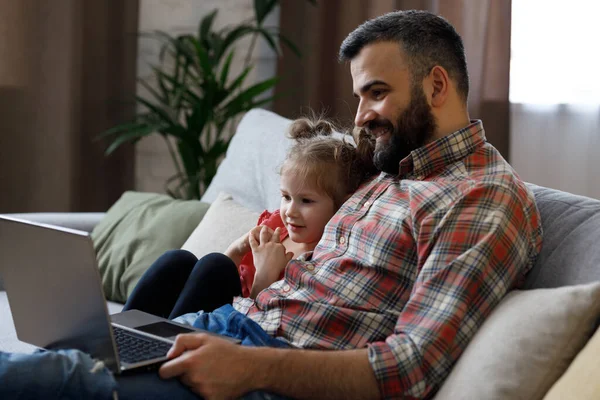 Father and daughter watching funny videos, browsing online tv on laptop with smile face. Happy family rest on coach with computer, enjoy spending time together on weekend at home. Fathers day.