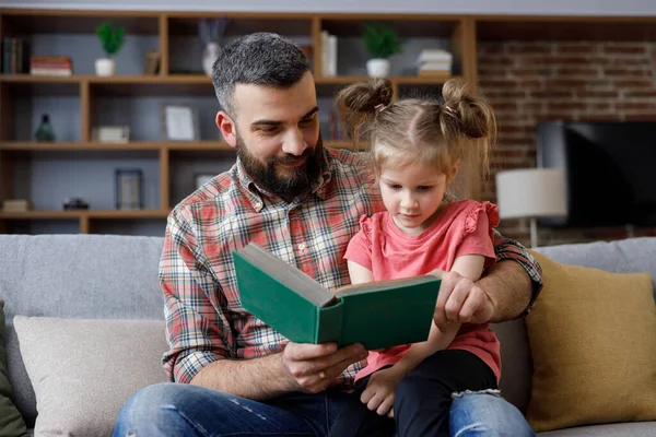 Young father and daughter read intersting book at home. Loving parent bearded man teaches his preschool child to read. Daddy reading fairy tale story. Parenthood, love and happy family concept.