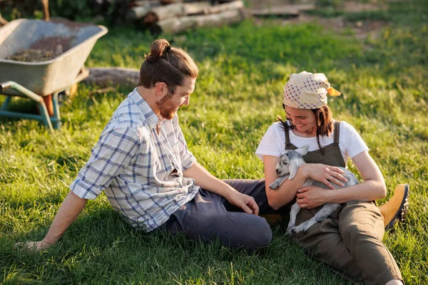 Portrait of young Caucasian happy farmer couple holding a little goat in their arms. Family business at ecological farm. Healthy food.Industrial production of goat milk dairy products. Cattle farming