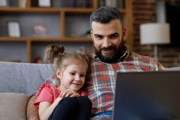 Father and daughter watching funny videos, browsing online tv on laptop with smile face. Happy family rest on coach with computer, enjoy spending time together on weekend at home. Fathers day.