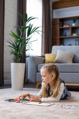 Çocuklar için eğitici oyuncaklar. Evdeki halının üzerinde renkli bloklar olan ahşap bir yapboz yapan sevimli küçük kız. Beyin oyuncular motor geliştirme ve mantıklı düşünme için oyuncak. Ev eğlencesi..