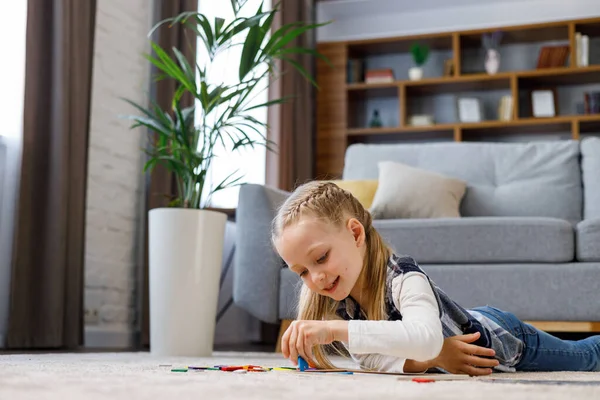 Educational toys for children. Cute little girl making a wooden puzzle with colorful blocks lying on the carpet at home. Brain teasers toy for motor development and logical thinking. Home leisure.