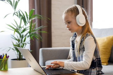 Evde dizüstü bilgisayar kullanarak okuyan tatlı bir ilkokul kızı. Ciddi çocuk ödevini yapıyor, online sınav sorularını cevaplıyor, sınavı geçiyor. Mesafe öğrenme. Çocuk evde eğitim.