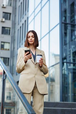 Genç bir esmer kız bir iş merkezinin arka planına karşı, ofis merkezine. Hareket halindeyken, akıllı telefonundan haberleri okuyor.