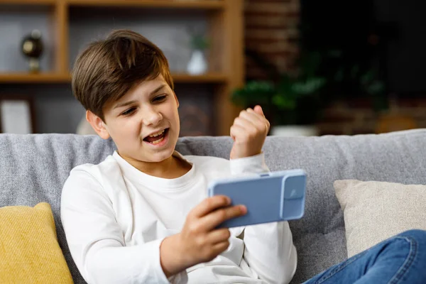 Teens and gaming addiction. Young boy playing video game on smartphone sitting on sofa at home. Cute teenager losing in car racing game on mobile phone. Spending time at home, leisure, relax.