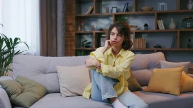 Tired curly girl falls down while sitting on the couch feeling apathy. Feeling depressed, lack of motivation, sadness, boredom. Exhausted, she collapses on the couch from stress