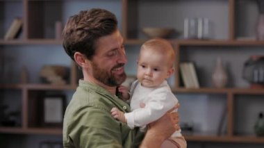 Close-up portrait of a father with a baby in his arms. Dad loves his little daughter, gently kisses. Father is on maternity leave. Paternity Leave. Paternal love.