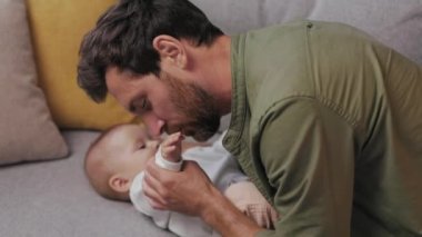 Dad plays with his little baby, on the couch in a cozy apartment. Fatherly love. Father hugs and kisses his little daughter.