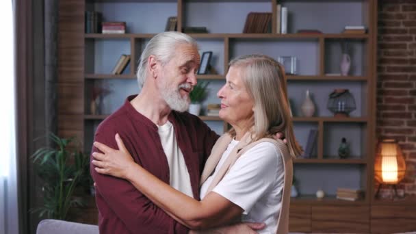 这对成熟快乐的夫妇低着头坐在沙发上 白头发的丈夫和妻子互相拥抱 快乐老年人的关系 中年祖父母一起在家里放松 — 图库视频影像
