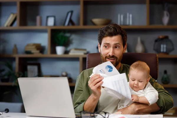 Father on maternity leave, holding an online conference, a meeting in the home office with a small child in his arms. Dad with a child. Freelancer combines child care and work. Paternity leave.