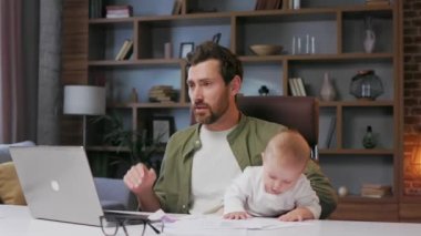 Father on maternity leave, holding an online conference, a meeting in the home office with a small child in his arms. Dad with a child. Freelancer combines child care and work. Paternity leave.