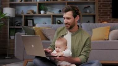 A young father, with a child, does housework. Father on maternity leave. Dad cheerfully sings, dances and vacuums, cleans with a small child in his arms. Paternity Leave.
