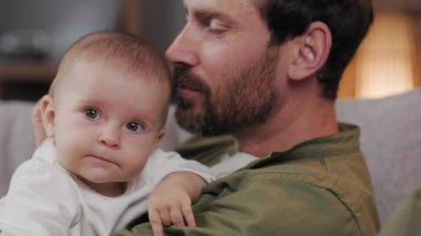 Dad plays with his little baby, on the couch in a cozy apartment. Fatherly love. Father hugs and kisses his little daughter.