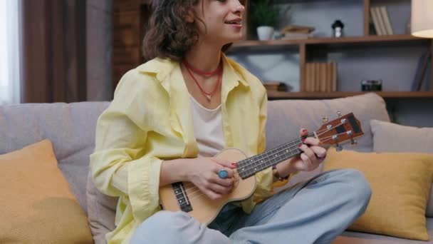 Beautiful Hipster Girl Yellow Shirt Plays Sings Ukulele Sofa Apartment — Stock video
