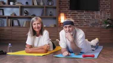 Gri saçlı, mutlu, olgun yaşlı çift evde jimnastik yapıyor. Emekliler için aktif ve sağlıklı bir yaşam tarzı. Fitness, eğlence, yaşlıların refahı.