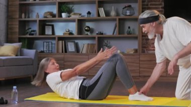 Gri saçlı, mutlu, olgun yaşlı çift evde jimnastik yapıyor. Emekliler için aktif ve sağlıklı bir yaşam tarzı. Fitness, eğlence, yaşlıların refahı.