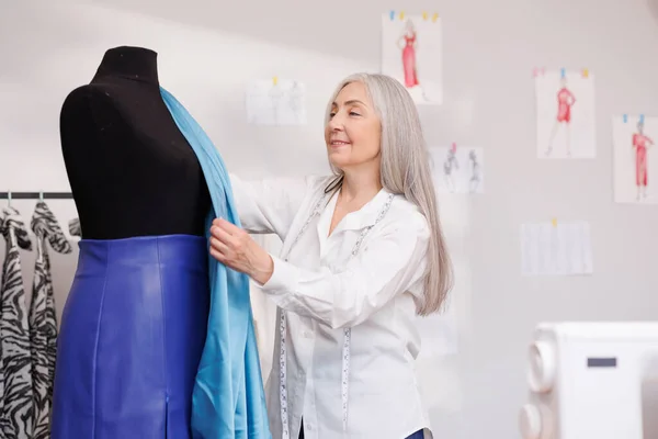 Woman with gray hair, fashion designer, stylist. Tries fabric on a mannequin. Designers home office