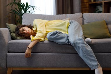 Tired curly girl falls down while sitting on the couch feeling apathy. Feeling depressed, lack of motivation, sadness, boredom. Exhausted, she collapses on the couch from stress.