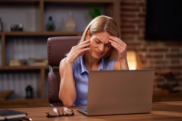 Exhausted woman feels eye fatigue after using laptop. In stress, an overworked woman takes off her glasses and massages her irritated eyes. Overworking, burnout.