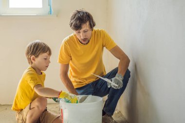 Oğluyla evde tamirat yapan bir adam, çocuklara ellerinde bir spatulayla duvarları alçılamayı öğretiyor.