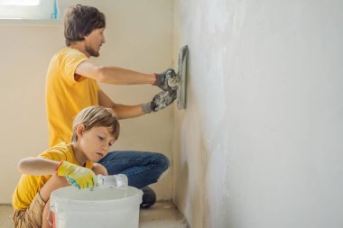 Oğluyla evde tamirat yapan bir adam, çocuklara ellerinde bir spatulayla duvarları alçılamayı öğretiyor.