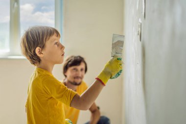 Oğluyla evde tamirat yapan bir adam, çocuklara ellerinde bir spatulayla duvarları alçılamayı öğretiyor.