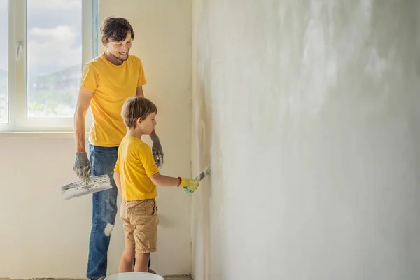 L'uomo con suo figlio fa riparazioni a casa, insegna ai bambini a intonacare le pareti con una spatola in mano. — Foto Stock