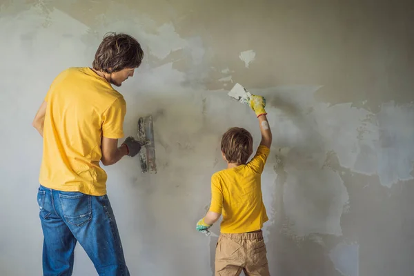 Mężczyzna z synem robi naprawy w domu, uczy dzieci tynkowania ścian z łopatką w rękach — Zdjęcie stockowe