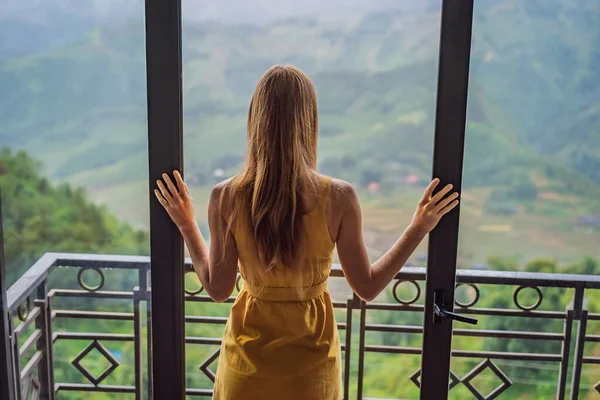 Młoda kobieta trzyma filiżankę kawy siedząc na krześle na balkonie, patrząc na góry i zieloną przyrodę. Kobieta w Sapa we mgle, północno-zachodni Wietnam. Pojęcie podróży do Wietnamu. Dziedzictwo UNESCO — Zdjęcie stockowe