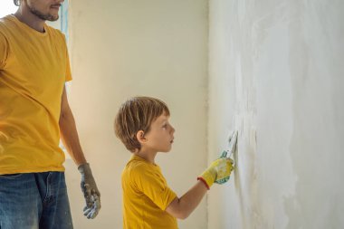 Oğluyla evde tamirat yapan bir adam, çocuklara ellerinde bir spatulayla duvarları alçılamayı öğretiyor.