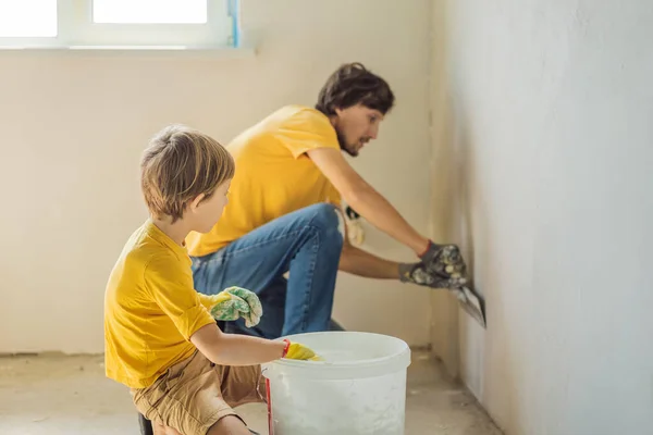 L'uomo con suo figlio fa riparazioni a casa, insegna ai bambini a intonacare le pareti con una spatola in mano. — Foto Stock