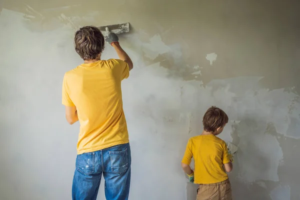 Az ember a fiával otthon javít, gyerekeket tanít arra, hogy ragasszák fel a falakat egy spatulával a kezében. — Stock Fotó