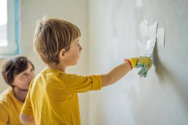 Oğluyla evde tamirat yapan bir adam, çocuklara ellerinde bir spatulayla duvarları alçılamayı öğretiyor.