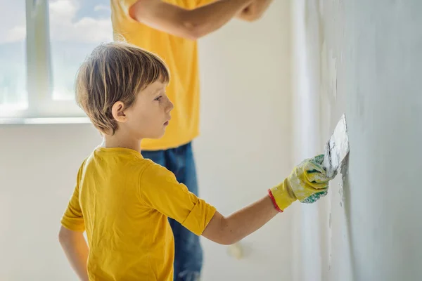 L'uomo con suo figlio fa riparazioni a casa, insegna ai bambini a intonacare le pareti con una spatola in mano. — Foto Stock