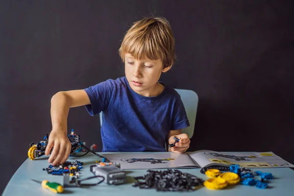 Veselý chytrý školák, který sedí u stolu a dělá doma robotické zařízení — Stock fotografie