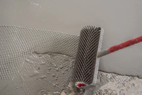 Gipser bei Bodenbelagsarbeiten mit selbstnivellierendem Zementmörtel, verwendet eine Nadelwalze — Stockfoto