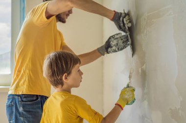 Oğluyla evde tamirat yapan bir adam, çocuklara ellerinde bir spatulayla duvarları alçılamayı öğretiyor.