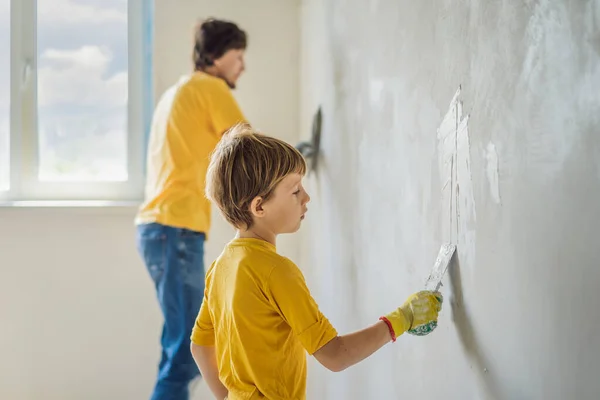 Man met zijn zoon repareert thuis, hij leert kinderen om de muren te pleisteren met een spatel in zijn handen — Stockfoto