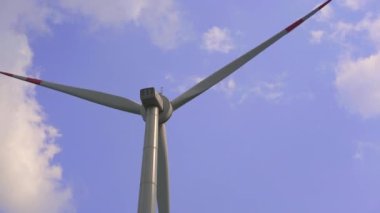 El kamerasıyla. Arka planda mavi bulutlu bir gökyüzü olan bir rüzgar enerjisi türbini. Yeşil enerjiye yatırım. Yeşil elektrik kavramı