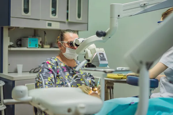Tandheelkundige behandeling met een microscoop. Een vrouw die tanden laat onderzoeken bij tandartsen. Afspraak bij de tandarts. lifestyle, het echte leven — Stockfoto
