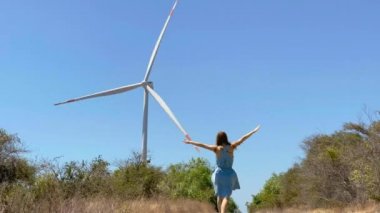 Rüzgâr jeneratörüne giden yolda duran bir kadının yavaş çekimi. Yeşil enerjiye yatırım. Yeşil elektrik kavramı