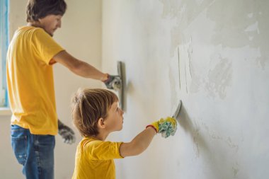 Oğluyla evde tamirat yapan bir adam, çocuklara ellerinde bir spatulayla duvarları alçılamayı öğretiyor.