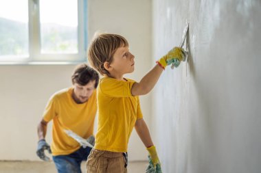Oğluyla evde tamirat yapan bir adam, çocuklara ellerinde bir spatulayla duvarları alçılamayı öğretiyor.