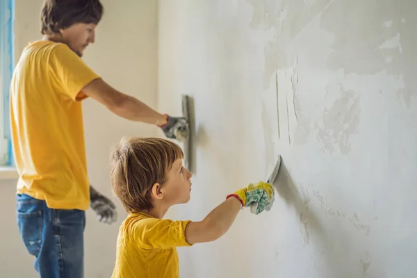 L'uomo con suo figlio fa riparazioni a casa, insegna ai bambini a intonacare le pareti con una spatola in mano. — Foto Stock