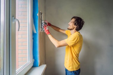 Sıvacı ev iyileştirme ustası macun bıçağıyla apartman duvarını doldurmaya çalışıyor.