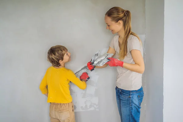 A nő, akinek hir fia van, javításokat végez otthon, megtanítja a fiút, hogyan vakolja be a falakat egy spatulával a kezében. — Stock Fotó