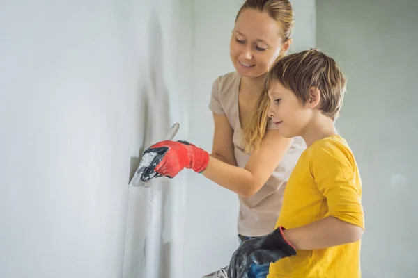 Donna con suo figlio fa riparazioni a casa, insegna al ragazzo a intonacare le pareti con una spatola in mano. — Foto Stock