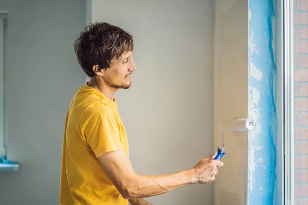 Ein männlicher Hausmaler arbeitet beim Streichen und Grundieren der Wand mit einer Malerrolle. Heimwerken — Stockfoto