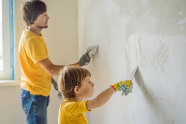 Oğluyla evde tamirat yapan bir adam, çocuklara ellerinde bir spatulayla duvarları alçılamayı öğretiyor..